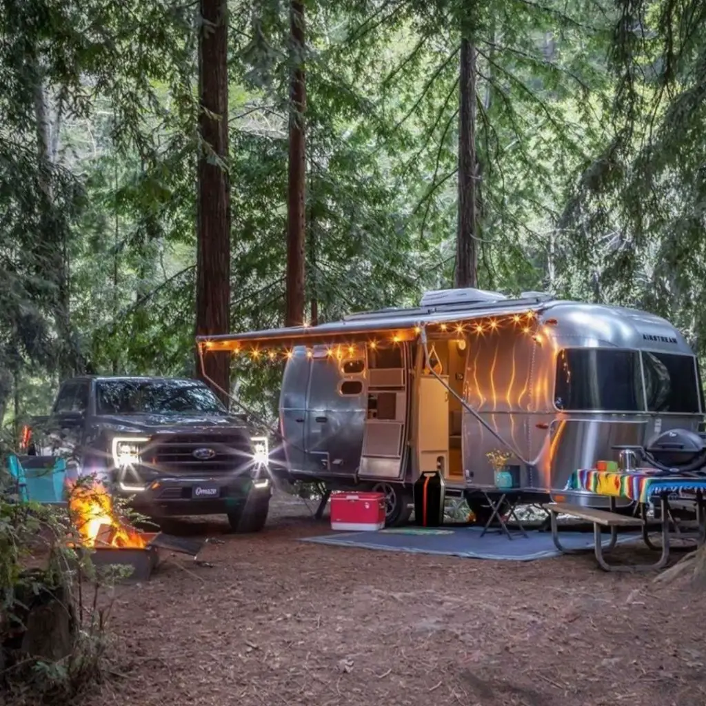 Airstream RV in a wooded campsite with a truck and CarGeneratror beside it - backup RV power